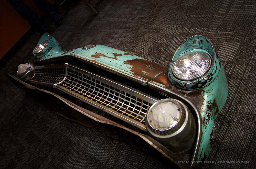 IMG_0701_ADM_Web_55FordCountrySedan_1000x661_200k+Tag A front end of a 1955 blue rusted Ford truck sits on the floor.